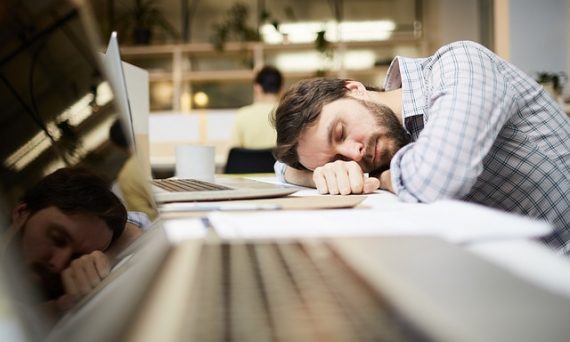 A person sleeping at a desk with a laptop and headphones, engaged in a video conference call with colleagues. They have a focused expression, with a professional and organized workspace in the background.