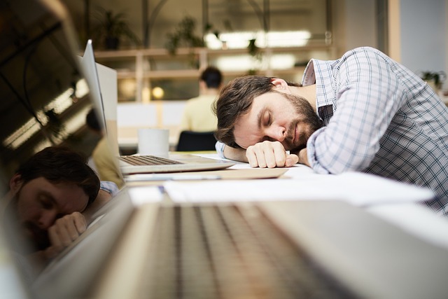 A person sleeping at a desk with a laptop and headphones, engaged in a video conference call with colleagues. They have a focused expression, with a professional and organized workspace in the background.